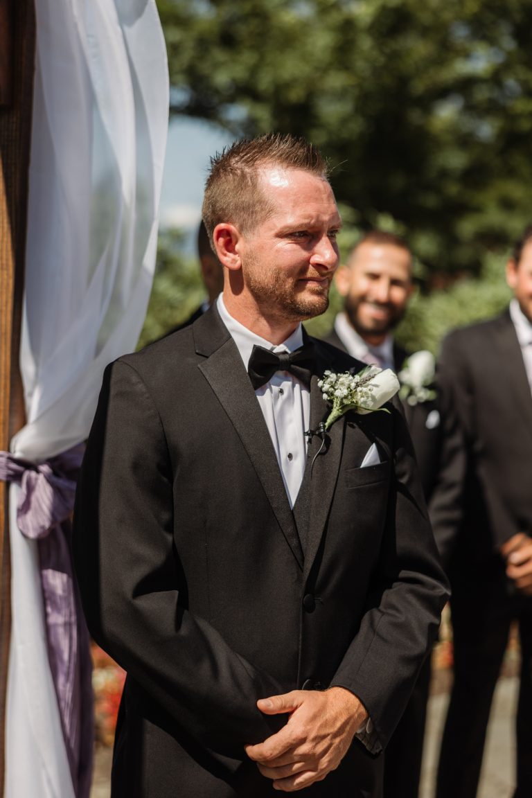 A groom waits at the front of the ceremony with his groomsmen